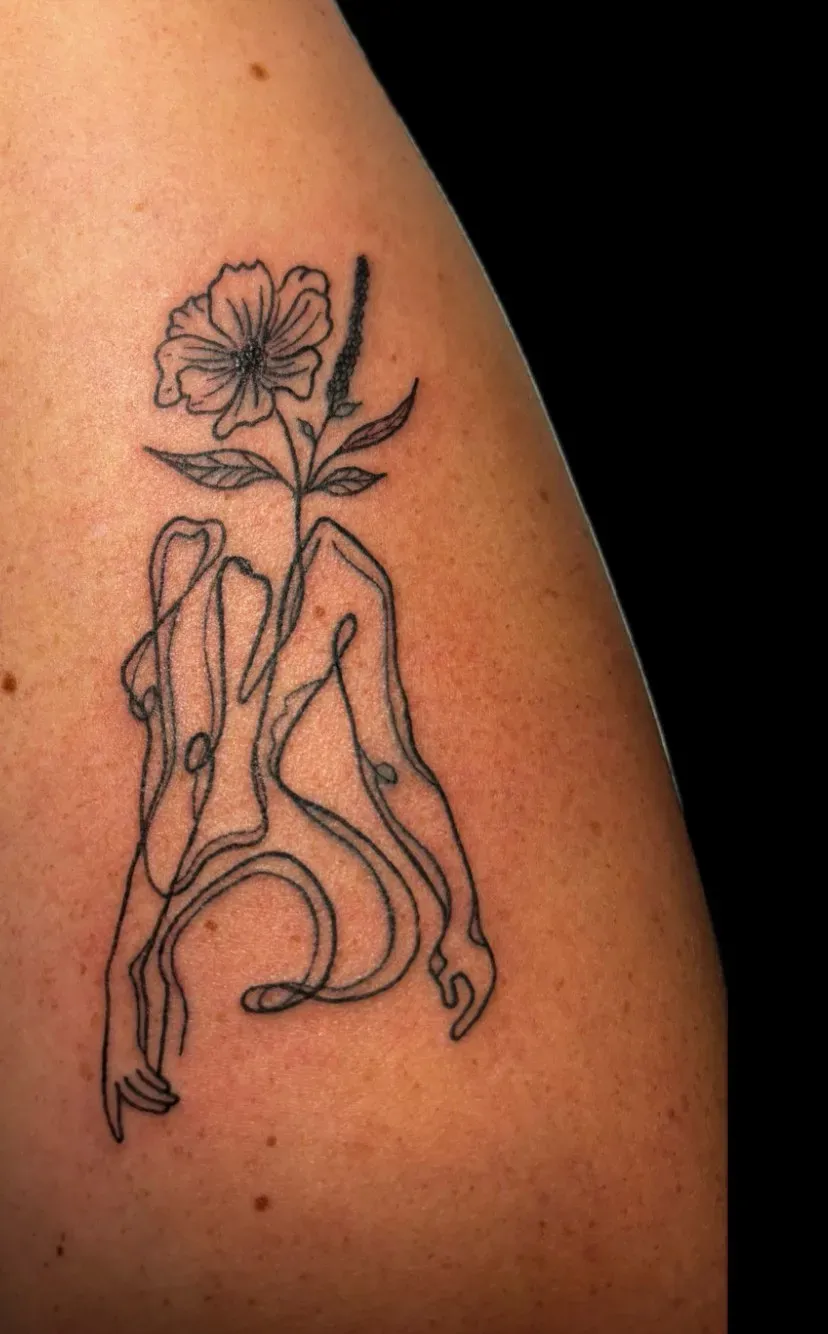 Fine line bloem met vrouwfiguur in doorlopende lijn op het bovenbeen, tattoo Gent