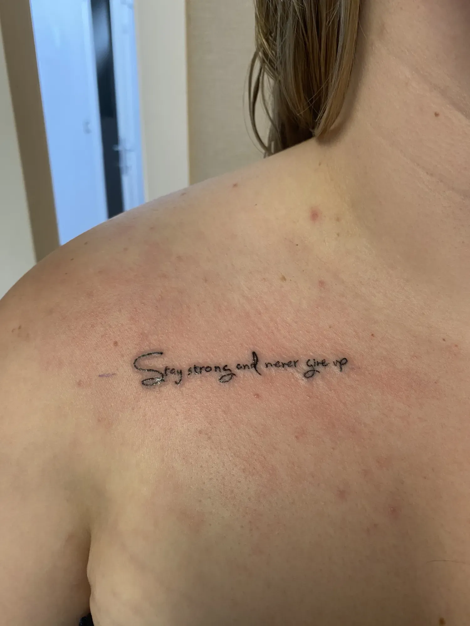 Fijne lettering Stay strong and never give up op het sleutelbeen, tattoo Gent